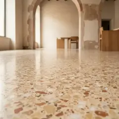 Pavimentazione terrazzo lucida con inserti colorati, che riflette la luce in un ambiente con archi e arredi in legno.