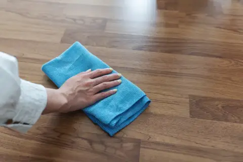 Mano con panno blu che pulisce un pavimento in legno, mostrando come togliere la colla dal legno con delicatezza.