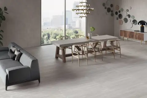 Un elegante soggiorno con divano grigio, tavolo da pranzo in cemento e sedie in legno, il tutto su un pavimento in gres porcellanato ruvido che evoca un'atmosfera moderna e accogliente.