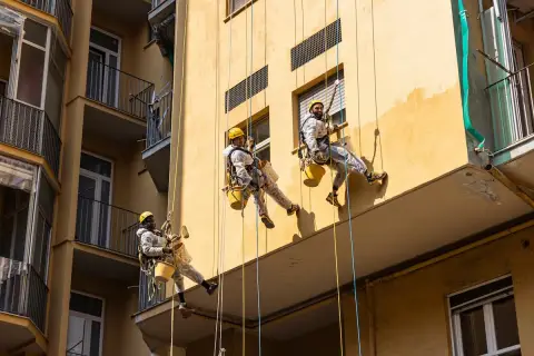 Operai in corda applicano il miglior intonaco per esterni su un edificio giallo. Lavori in quota per un risultato impeccabile.
