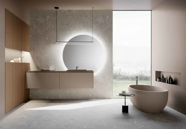 Bagni moderni con eleganti piastrelle effetto pietra. Vasca ovale, mobile sospeso e specchio luminoso creano un'oasi di relax.