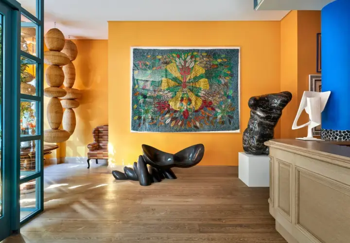 Un soggiorno vibrante con pareti arancioni che esaltano gli effetti pittura pareti moderne. Sculture audaci e un arazzo colorato creano un'atmosfera artistica.