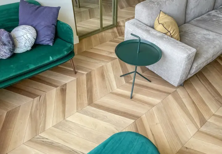 Un elegante soggiorno con un pavimento stile nordico a spina di pesce. Divani verdi e grigi, tavolino verde e cuscini decorativi.