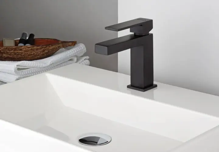 Lavabo bianco moderno con rubinetteria nera opaca. Accanto, asciugamani bianchi e una ciotola con prodotti da bagno.