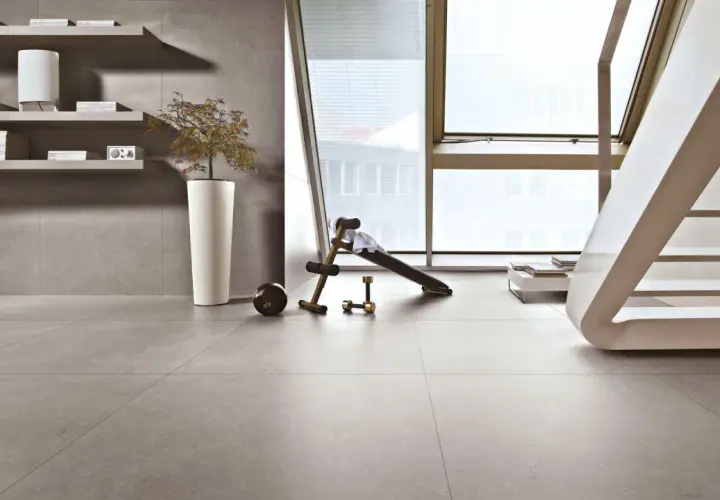 Pavimenti in kerlite per esterni, un angolo fitness con panca e pesi, scaffali con libri e una pianta in vaso.
