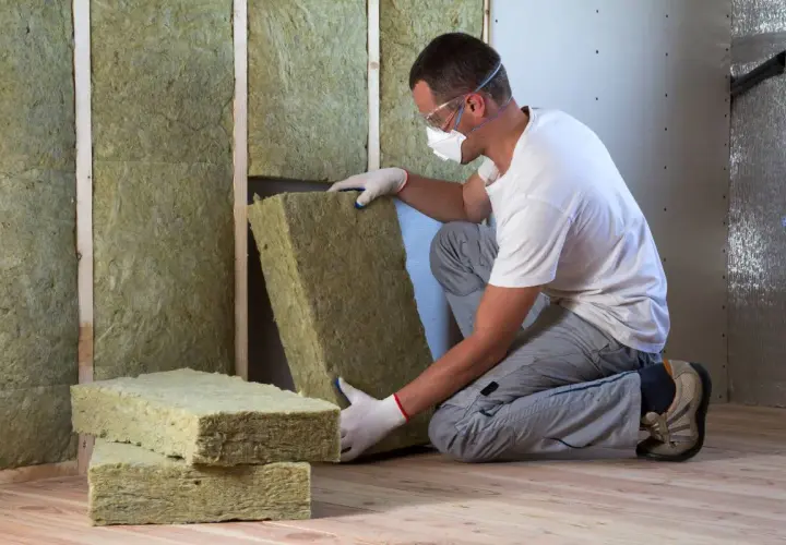 Operaio con maschera e occhiali installa pannelli di cappotto interno lana di roccia per isolare una parete.