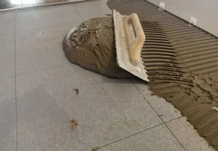 Cazzuola stende cemento per incollare piastrelle grigie. Lavoro in corso.