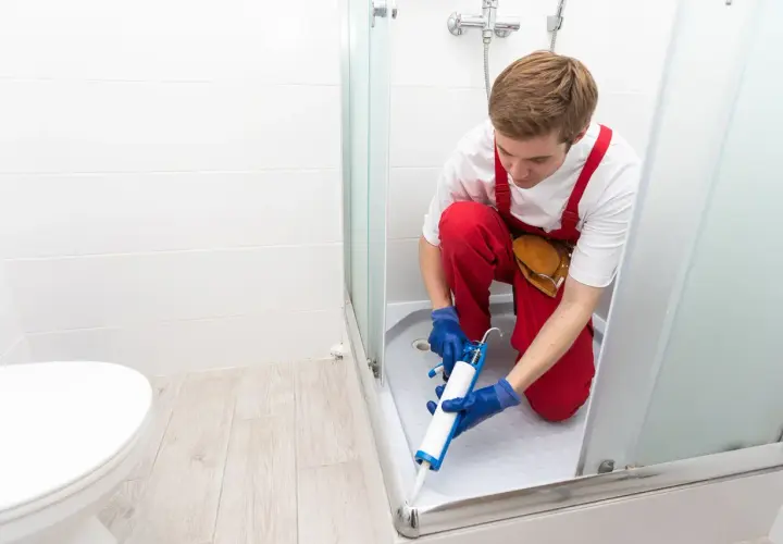 Installatore usa silicone per box doccia, sigillando la base per prevenire perdite d'acqua.
