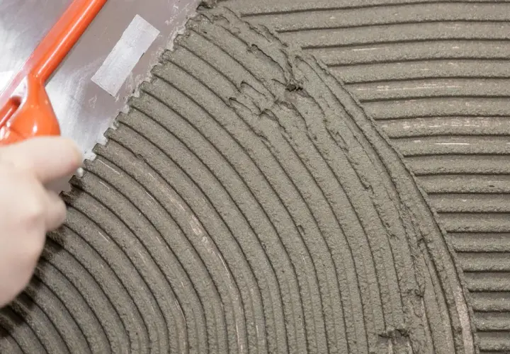 Una spatola dentata stende la colla per piastrelle su una superficie, creando righe uniformi per una posa perfetta.