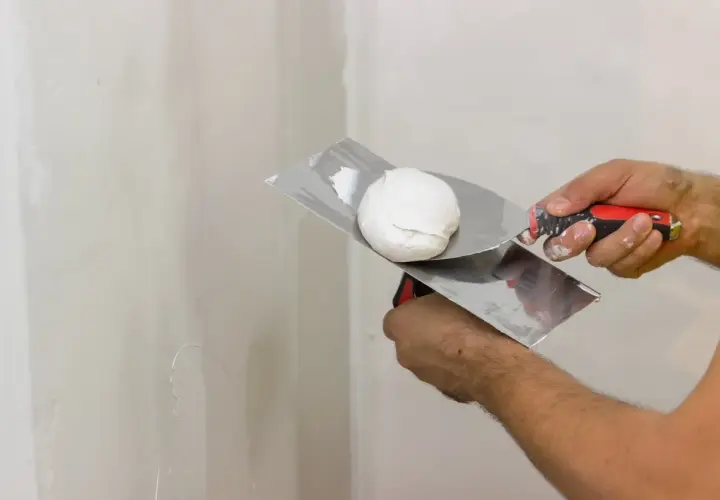 Mani esperte pronte a stuccare muro con spatola e stucco bianco.