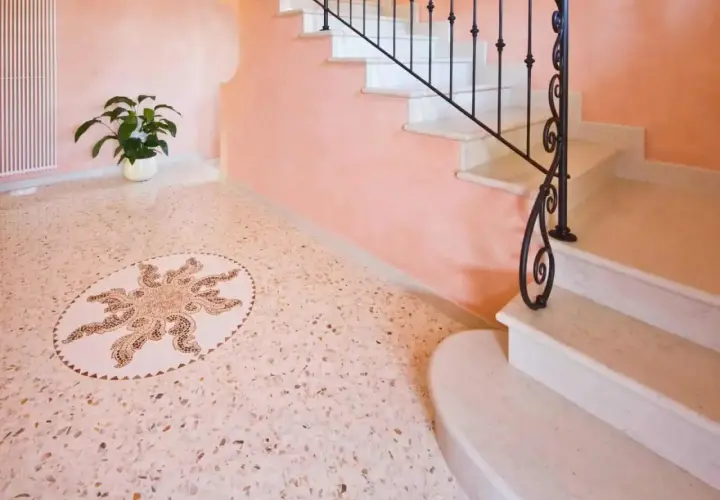 Un elegante pavimento veneziana con un mosaico centrale a forma di sole, accanto a una scala in marmo con ringhiera in ferro battuto.