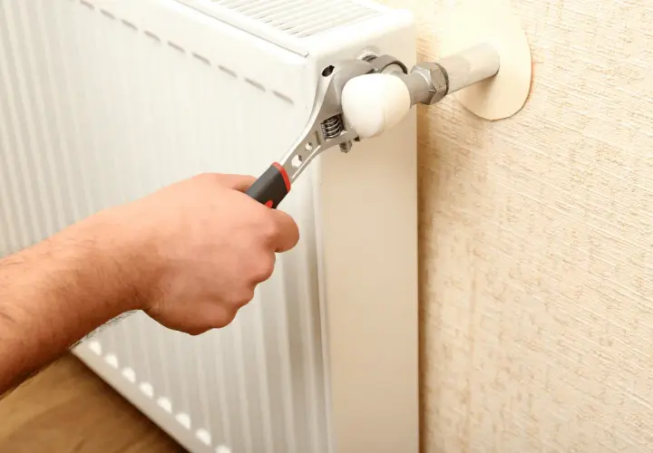 Mano con chiave inglese che regola un termosifone. L'aria nei termosifoni è un problema comune.
