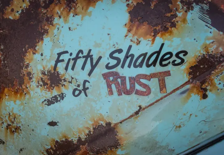 Superficie metallica sbiadita con scritte "Fifty Shades of RUST". La ruggine, che sembra voler togliere il colore originale, crea un effetto visivo intenso.