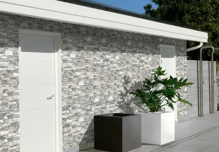 Muro esterno con rivestimento in pietra, che mostra diversi tipi di mattoni per muri esterni. Due porte bianche e fioriere moderne completano la scena.