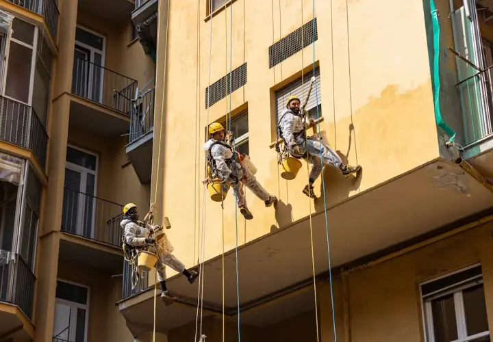 Operai in corda applicano il miglior intonaco per esterni su un edificio giallo. Lavori in quota per un risultato impeccabile.