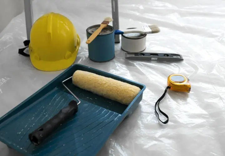 Attrezzi da lavoro: casco giallo, rullo, pennelli, livella, metro e barattoli di vernice, pronti per applicare l'intonaco per umidità.