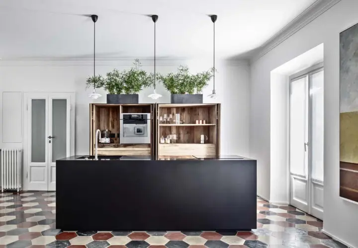 Cucina moderna con isola nera, pensili in legno, piante e pavimento con cementine esagonali colorate.