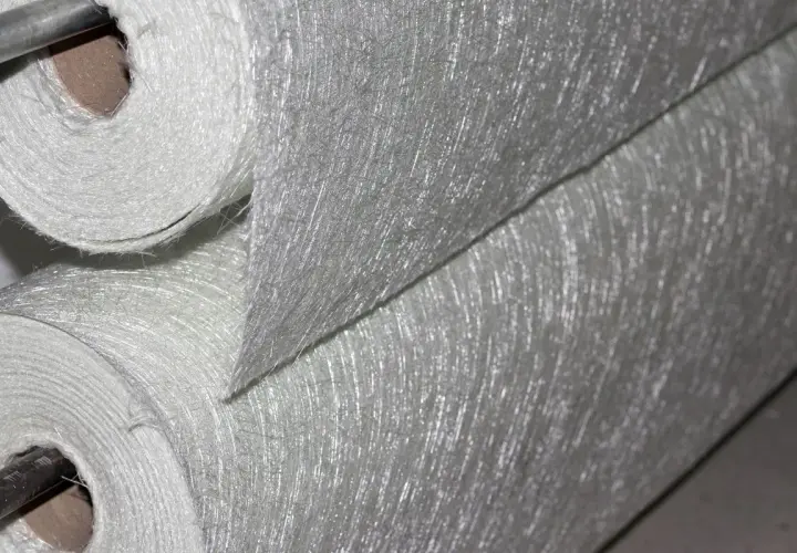 Rotoli di tessuto di fibra di vetro, materiale noto per la sua potenziale fibra di vetro cancerogena, con filamenti sottili e lucidi visibili.