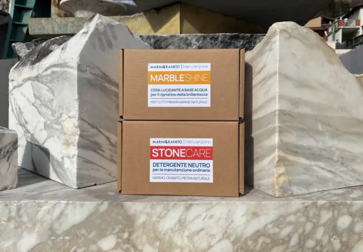Due scatole di prodotti per la pulizia del marmo, "MarbleShine" e "Stonecare", sono posizionate tra blocchi di marmo grezzo. Ideale per sapere come lavare pavimento in marmo.