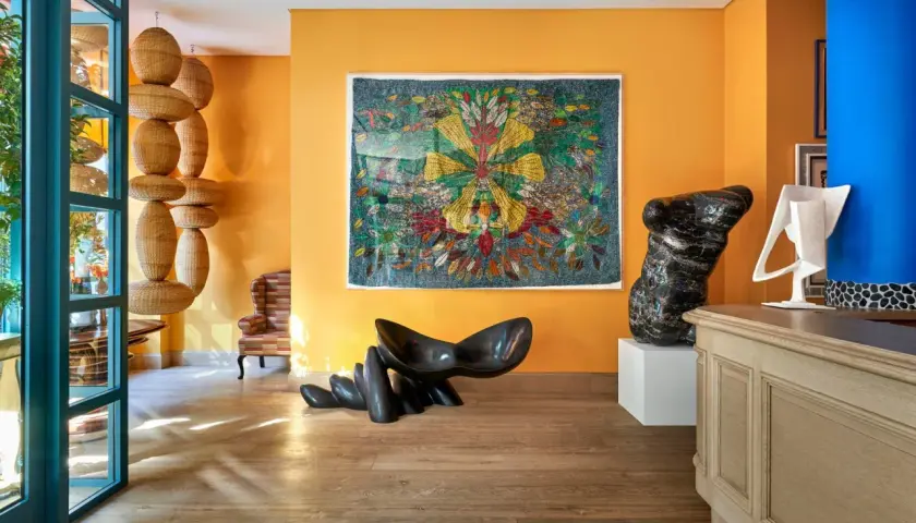Un soggiorno vibrante con pareti arancioni che esaltano gli effetti pittura pareti moderne. Sculture audaci e un arazzo colorato creano un'atmosfera artistica.