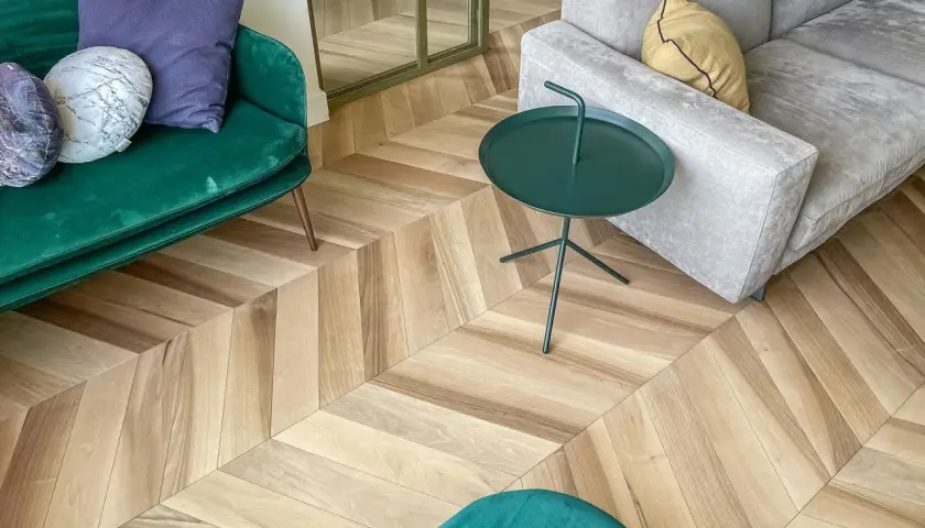 Un elegante soggiorno con un pavimento stile nordico a spina di pesce. Divani verdi e grigi, tavolino verde e cuscini decorativi.