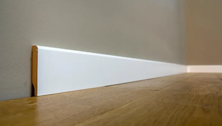 Battiscopa bianco moderno, con un'altezza che definisce lo spazio. Il legno del pavimento riflette la luce.
