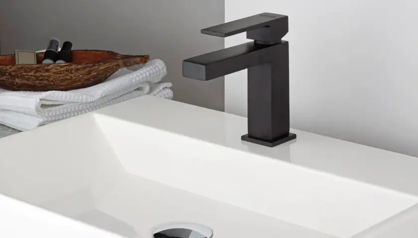 Lavabo bianco moderno con rubinetteria nera opaca. Accanto, asciugamani bianchi e una ciotola con prodotti da bagno.