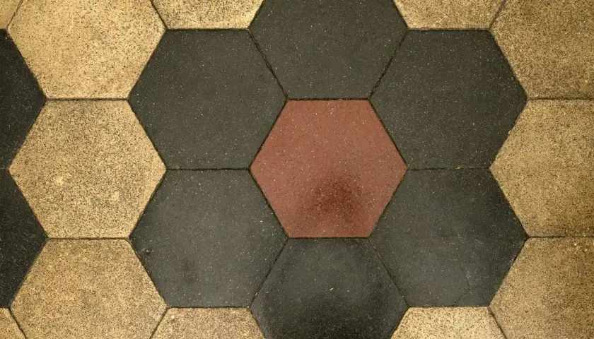 Pavimentazione a nido d'ape con cementine esagonali color ocra, grigio scuro e un tocco di rosso.