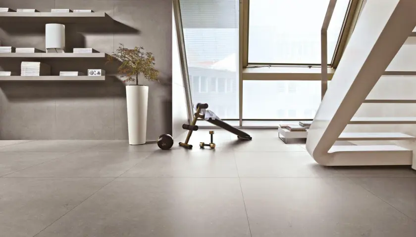 Pavimenti in kerlite per esterni, un angolo fitness con panca e pesi, scaffali con libri e una pianta in vaso.