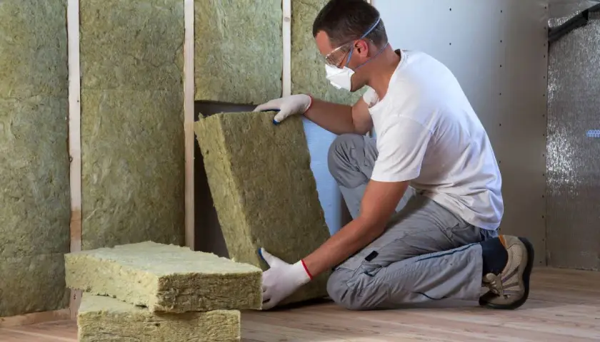 Operaio con maschera e occhiali installa pannelli di cappotto interno lana di roccia per isolare una parete.