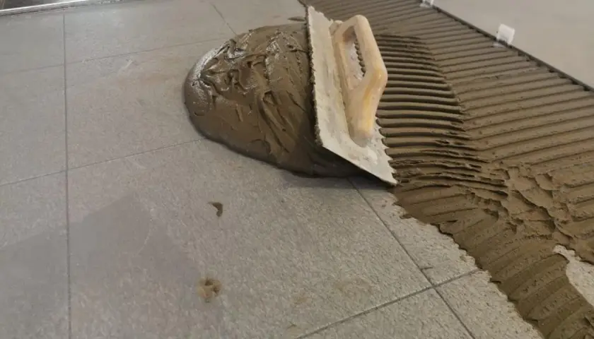 Cazzuola stende cemento per incollare piastrelle grigie. Lavoro in corso.