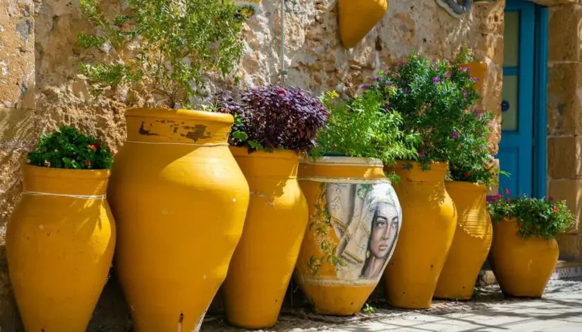 Vasi gialli dipinti e grezzi, alcuni con piante rigogliose, raccontano la storia della ceramica in un vicolo soleggiato.