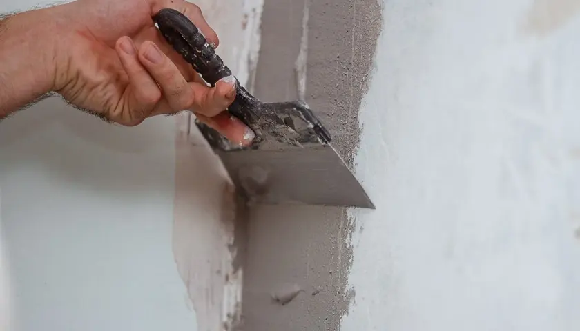 Mano usa una spatola per applicare materiale per chiudere buchi nel muro.