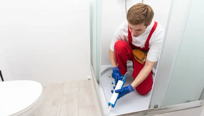 Installatore usa silicone per box doccia, sigillando la base per prevenire perdite d'acqua.