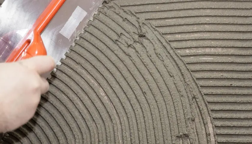 Una spatola dentata stende la colla per piastrelle su una superficie, creando righe uniformi per una posa perfetta.
