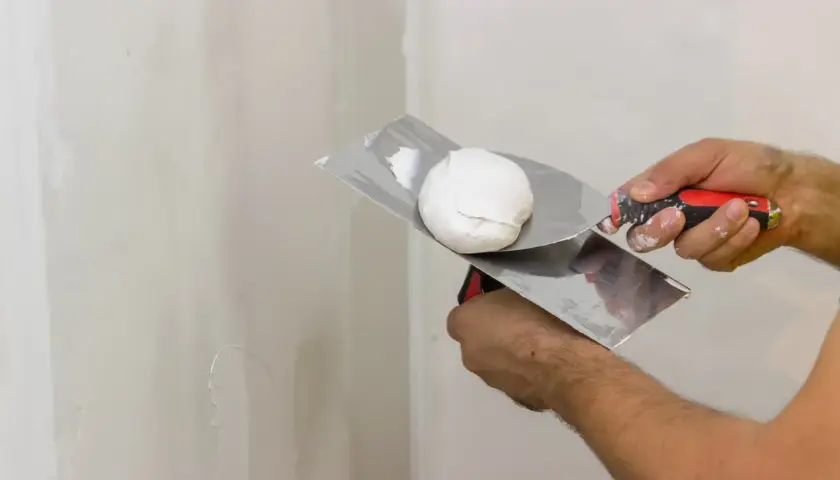 Mani esperte pronte a stuccare muro con spatola e stucco bianco.