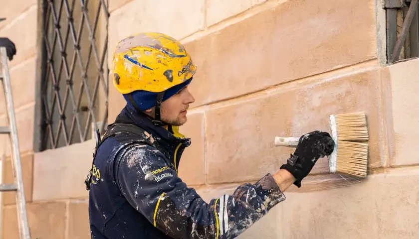 Operaio con casco giallo applica intonaco a un muro, un'alternativa alla rasatura dei muri per un nuovo look.