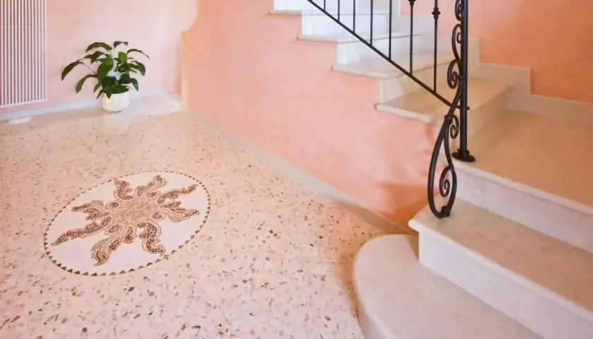 Un elegante pavimento veneziana con un mosaico centrale a forma di sole, accanto a una scala in marmo con ringhiera in ferro battuto.