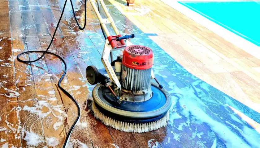 Macchina lavapavimenti in azione su un deck di legno, rimuovendo efficacemente la polvere di muratura e lo sporco, vicino a una piscina.