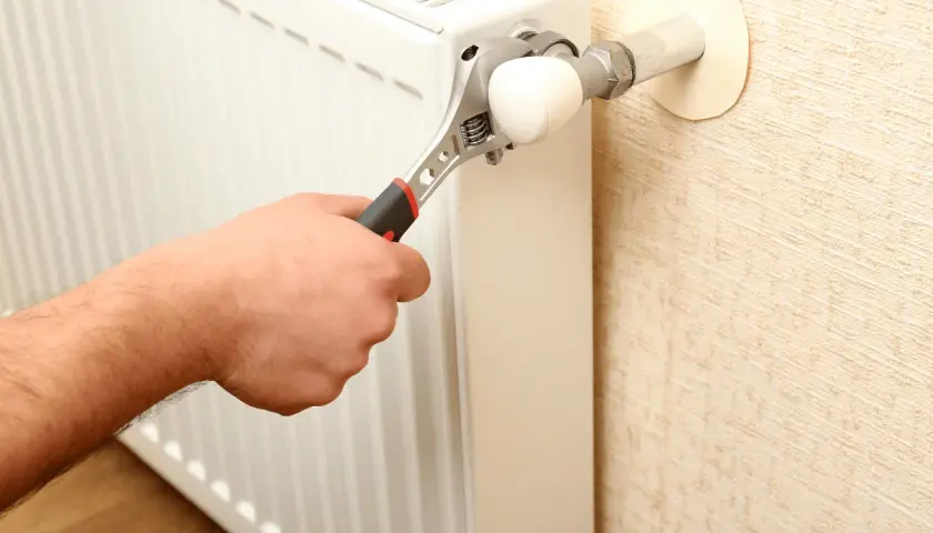 Mano con chiave inglese che regola un termosifone. L'aria nei termosifoni è un problema comune.