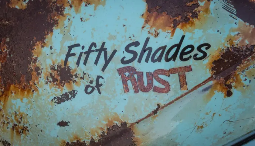 Superficie metallica sbiadita con scritte "Fifty Shades of RUST". La ruggine, che sembra voler togliere il colore originale, crea un effetto visivo intenso.