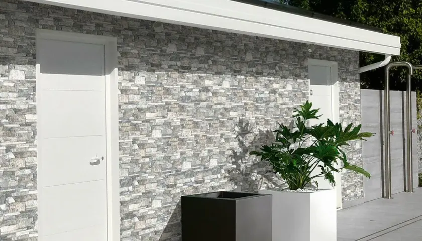 Muro esterno con rivestimento in pietra, che mostra diversi tipi di mattoni per muri esterni. Due porte bianche e fioriere moderne completano la scena.
