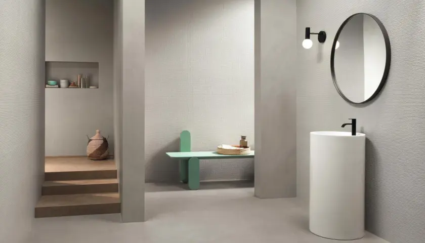 Bagno moderno con rivestimento uguale al pavimento, lavabo a colonna, specchio rotondo e nicchia con oggetti decorativi.