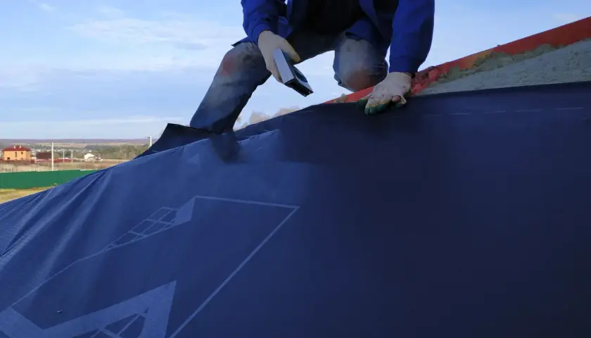 Installazione di una barriera al vapore su un tetto. La scheda tecnica del materiale è visibile.