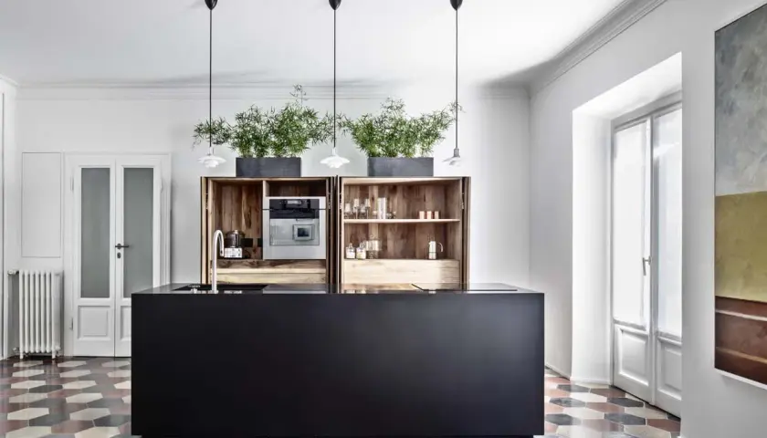 Cucina moderna con isola nera, pensili in legno, piante e pavimento con cementine esagonali colorate.
