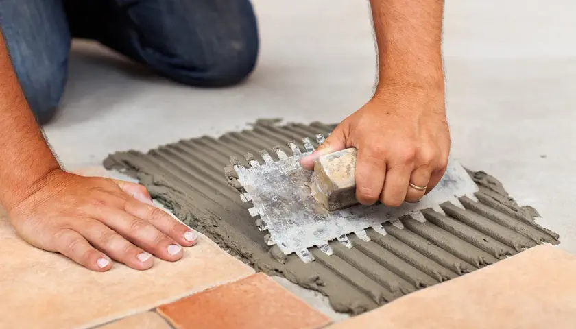 Mani esperte stendono la colla per piastrelle con una spatola dentata, creando un letto uniforme. La quantità di colla per piastrelle al mq è fondamentale per una posa perfetta.