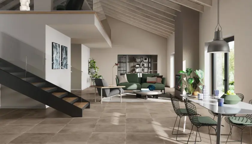 Pavimento con effetto cemento in un soggiorno moderno con scala a vista, divano verde e zona pranzo.