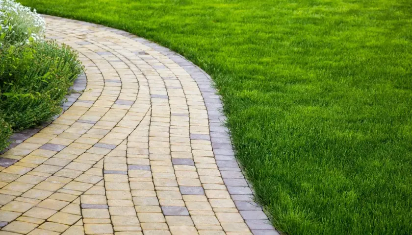 Un vialetto carrabile economico in pavé curvo, fiancheggiato da un prato verde brillante e vegetazione rigogliosa.