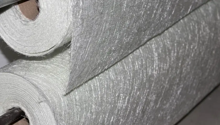Rotoli di tessuto di fibra di vetro, materiale noto per la sua potenziale fibra di vetro cancerogena, con filamenti sottili e lucidi visibili.