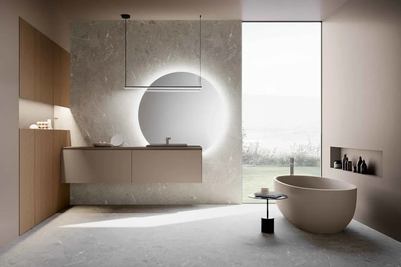 Bagni moderni con eleganti piastrelle effetto pietra. Vasca ovale, mobile sospeso e specchio luminoso creano un'oasi di relax.